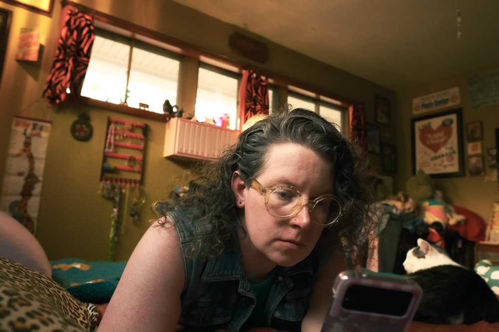A of Temperance laying in bed in her bedroom looking at her phone. Her cat Mr. Mouse lays next to her