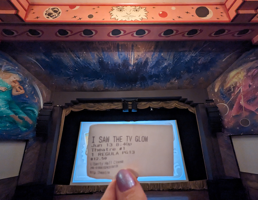 A ticket stub to I Saw the TV Glow pictured in an otherworldly theater with celestial murals on the walls and moons painted on the ceiling.