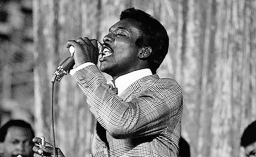 Wilson Pickett in a plaid suit, belting into a microphone.